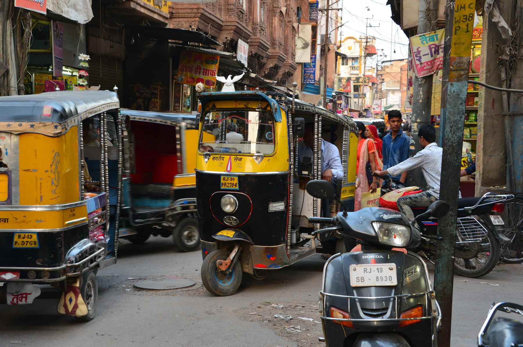 Auto-rickshaws and scooters sharing a narrow commercial street in Jodhpur in 2016