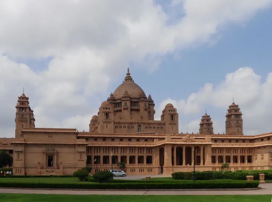 Sandstone facade and central dome of Umaid Bhawan Palace beneath a cloudy sky.